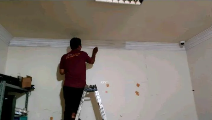 Teknisi merapikan bidang plafon dan dinding sebelum pengecatan ulang area bekas rembesan