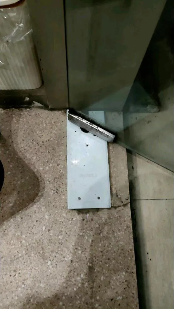 Pelat dudukan bawah pintu kaca yang dilepas saat proses bongkar-pasang, disandarkan pada daun kaca di area lobby